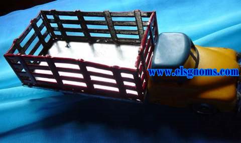 Camin fabricado en Portugal en hojalata embutida en prensa y troquelada. Cabina pintada en azul (cabina) y amarillo (cap). Soporte (suelo) pintado en gris y caja troquelada en forma de reja pintada exterior en rojo e interior blanco. Frontal y ruedas con restos de estao.